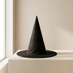 A black felt witch hat with a wide brim, displayed on a white pedestal against a warm beige wall near a window.