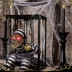 A Halloween decoration featuring a seated skeleton figure in a black-and-white striped prisoner outfit inside a black cage, with glowing red eyes. The scene is styled with fake cobwebs, black candlesticks, and spooky corner graphics.
