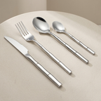 A 4-piece stainless steel cutlery set with a bamboo-inspired textured handle design, including a knife, fork, spoon, and teaspoon, arranged diagonally on a beige surface.