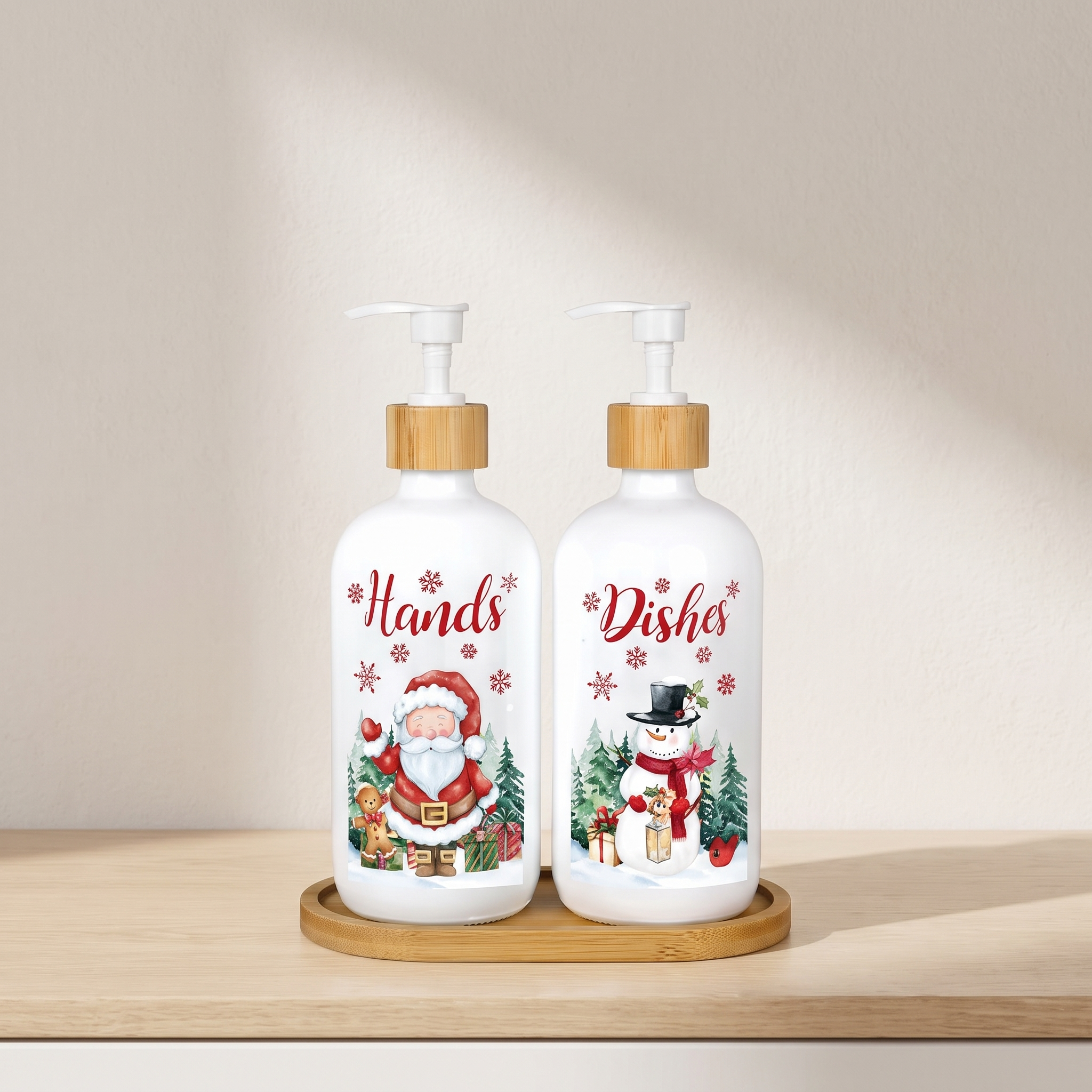 Two white pump bottles with bamboo caps sit on a round wooden tray on a light wood shelf. The left bottle is labeled 'Hands' and shows a Santa Claus illustration, while the right bottle is labeled 'Dishes' and shows a snowman illustration.