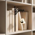 A small hanging ghost-shaped lamp with a black metal bracket and chain, displayed on a white bookshelf beside books.