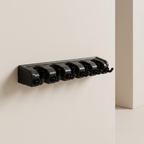 A black wall-mounted hook rack with six curved hooks, shown mounted on a warm off-white wall in a minimalist interior setting.