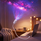 A white galaxy projector lamp on a bedside table casting a colorful starry night sky pattern onto the wall above a bed with a laptop and mug.