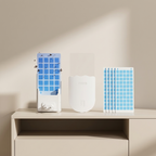 A white electronic pest trap device with blue grid panels, shown alongside a clear cover and a stack of adhesive blue grid filters on a beige shelf against a beige wall.