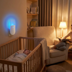 A white smart sleep monitor device glows with blue light on a wall above a baby crib where a baby is sleeping, while a woman reads in a cozy armchair in the background.