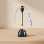 A modern desk lamp with a black conical base, a gold neck accent, and a black vertical stem. A flexible translucent sweep arm arches over the top, and a striped wand-like arm glows with blue and purple LED light.