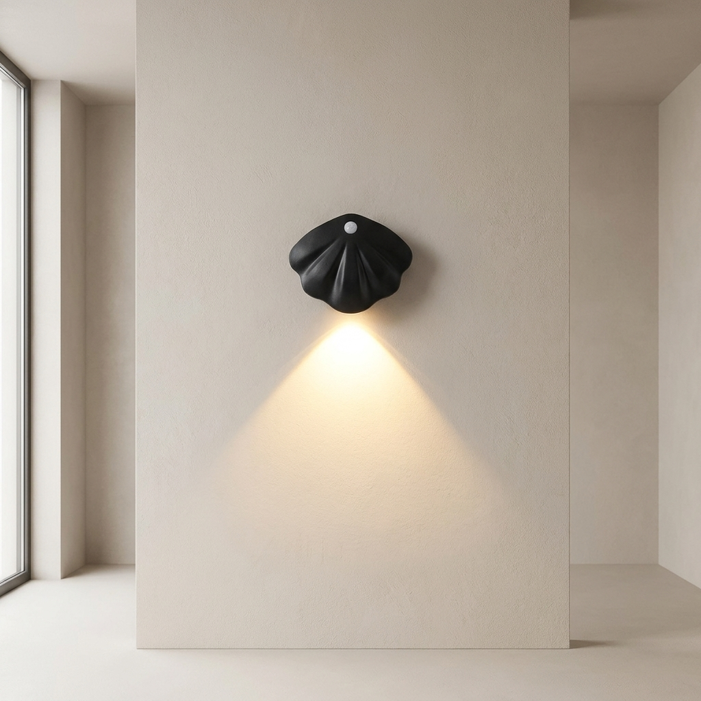 A black sculptural wall sconce with a shell-like form, mounted on a beige plaster wall and casting a warm downward light in a minimalist interior setting.