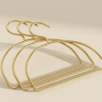 Three gold metal hangers arranged overlapping on a warm beige background.