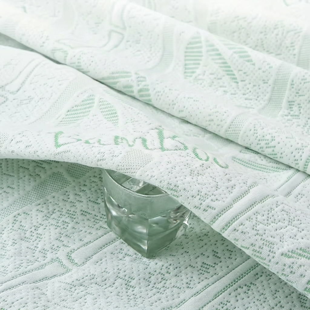 A close-up of a pale mint green textured fabric with a woven bamboo leaf pattern and the word 'bamboo' embroidered across it, with a faceted clear glass placed on top.