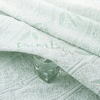 A close-up of a pale mint green textured fabric with a woven bamboo leaf pattern and the word 'bamboo' embroidered across it, with a faceted clear glass placed on top.