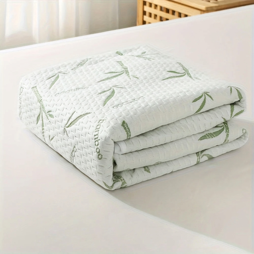 A folded white quilted mattress protector or comforter with a green bamboo leaf pattern, displayed on a white bed surface.