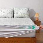 Bed with bamboo patterned pillows and a fitted sheet, nightstand with lamp in the background