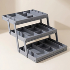 A three-tier gray plastic organizer tray with multiple compartments, shown on a clean beige background.