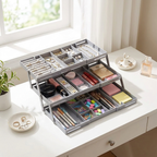 A gray metal jewelry organizer with multiple drawers and compartments, shown open on a white desk in a bright room. The organizer is filled with rings, necklaces, earrings, cosmetics, and stationery.