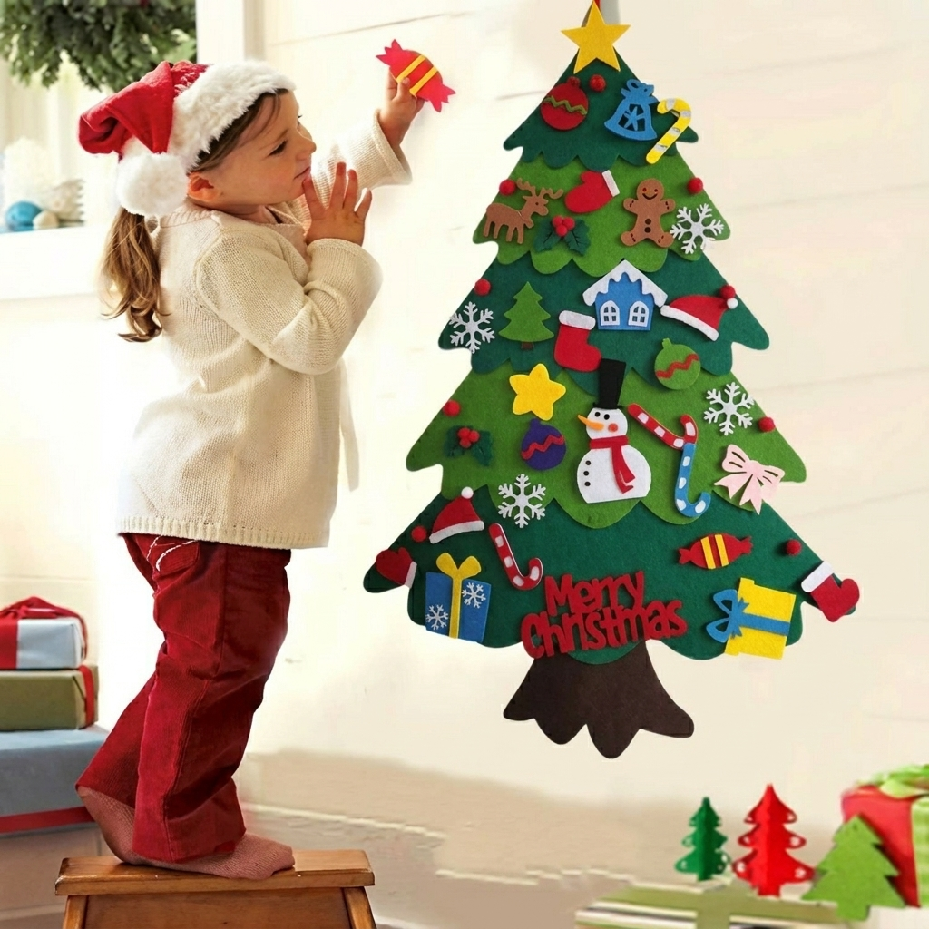 A child wearing a Santa hat and white sweater stands on a wooden stool, decorating a large felt Christmas tree with colorful holiday embellishments. The scene is indoors against a light wall, with small gift boxes and green felt trees on the floor.
