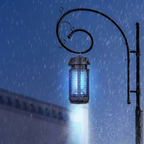 A hanging electric fly trap light with a glowing blue cage and bright downward beam, shown outdoors in the rain against a dark blue night sky.