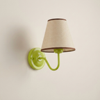 A wall-mounted sconce with a bright lime green metal wall plate and curved arm, paired with a tapered beige fabric shade trimmed in dark brown.