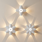 Three white flower-shaped wall sconces mounted on a beige wall, each casting a warm yellow light in a starburst pattern.