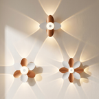 Three flower-shaped wall sconces with white petals and warm copper-brown centers, mounted on a beige wall and casting soft light beams.