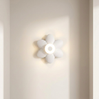 A white flower-shaped wall sconce with a glowing circular center, mounted on a warm beige wall.