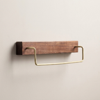 A wall-mounted bathroom towel bar with a rectangular wood backplate and a curved brass metal loop, shown against a plain light beige wall.