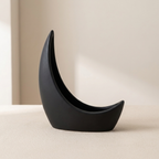 A matte black crescent moon-shaped decorative planter or dish, shown on a light beige surface against a neutral cream background.