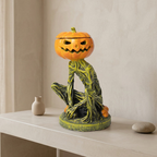 A Halloween-themed ceramic figurine of a seated green tree-like creature with a carved orange pumpkin head, displayed on a light beige console table against a neutral wall.
