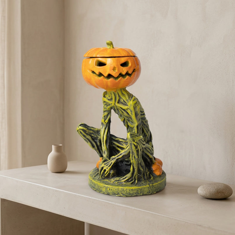 A Halloween-themed ceramic figurine of a seated green tree-like creature with a carved orange pumpkin head, displayed on a light beige console table against a neutral wall.