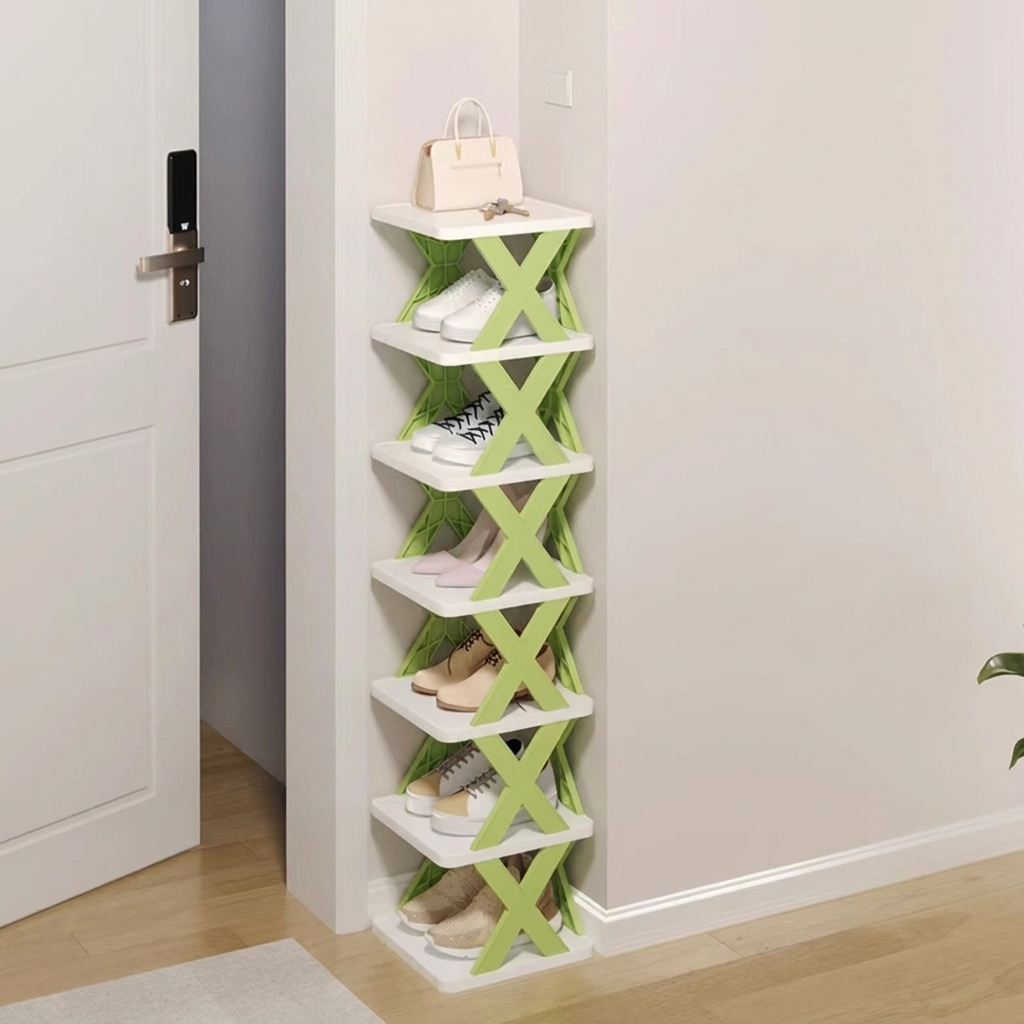 A slim, multi-tier shoe rack with white shelves and green X-shaped supports, shown in a hallway next to a white door. The rack is styled with various pairs of shoes and a handbag.