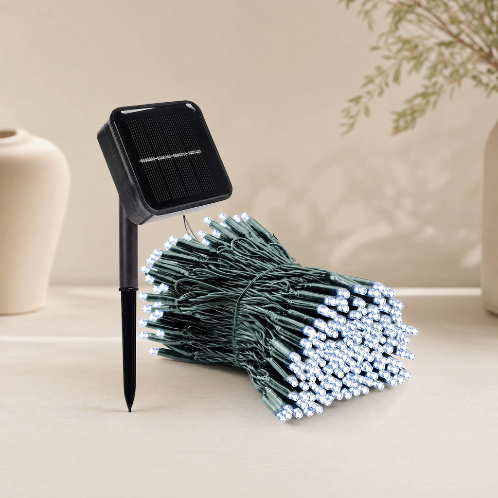 Solar garden string lights with a black solar panel stake and a bundle of green wire lights with white LED bulbs, displayed on a light beige surface.