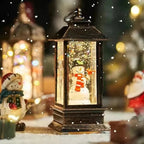 A dark brown lantern-style Christmas ornament with a glowing snowman figure inside, surrounded by festive blurred lights and snowfall effects.