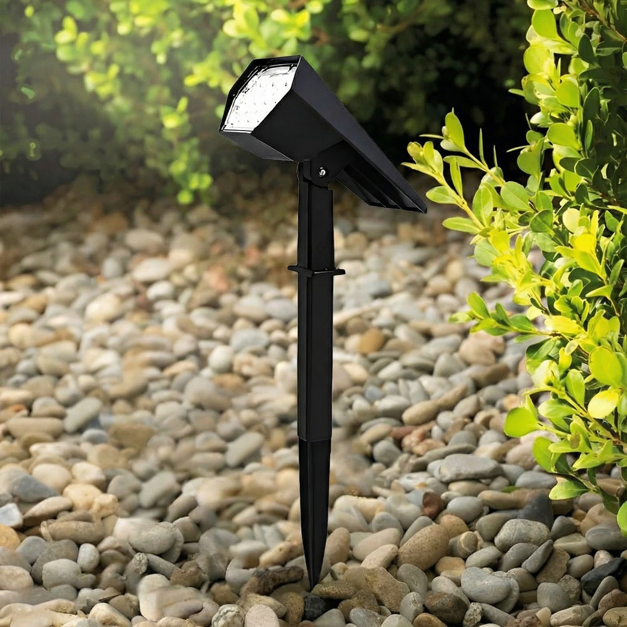 Black outdoor solar lamp on pebbles with greenery in the background
