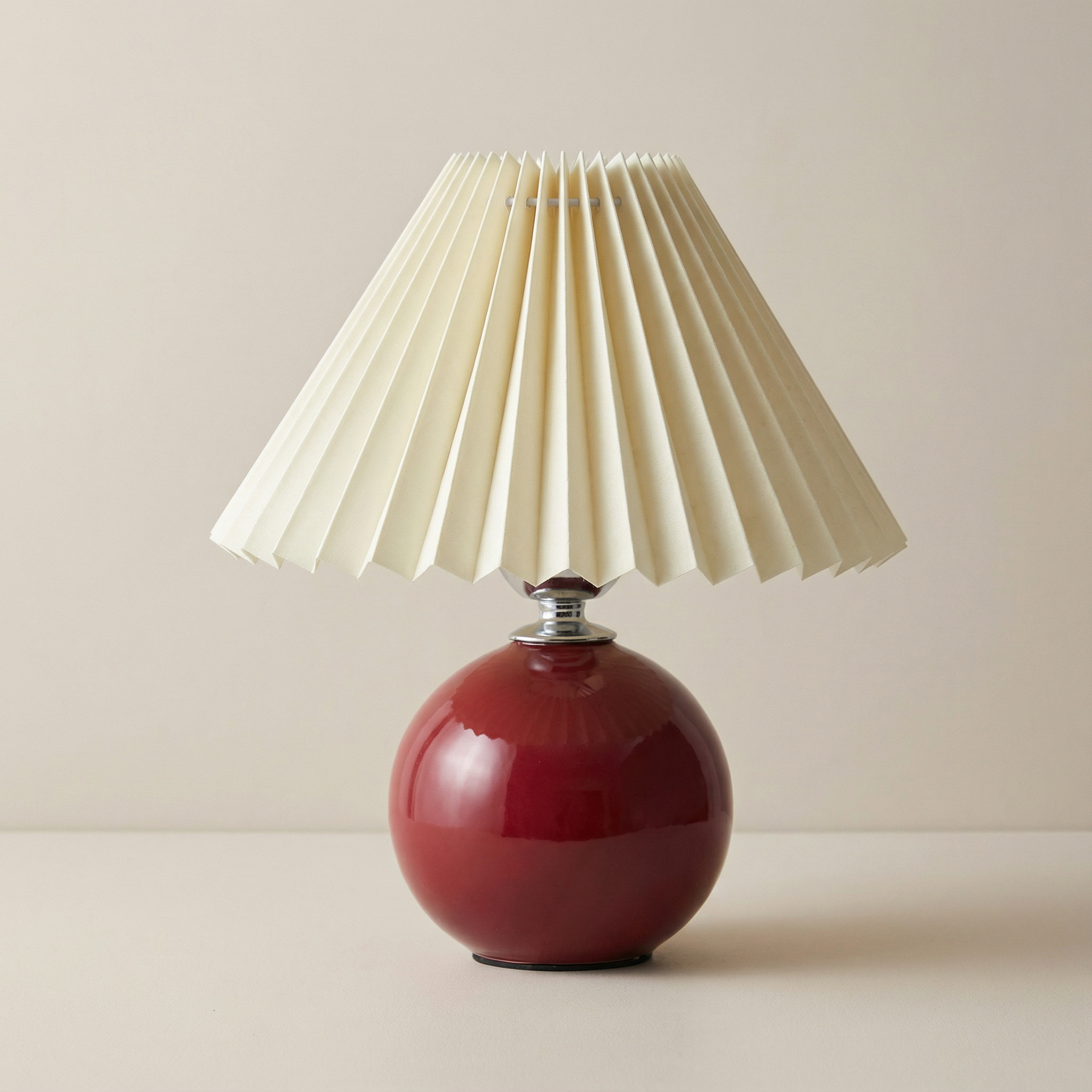 Red table lamp with a pleated beige shade on a neutral background