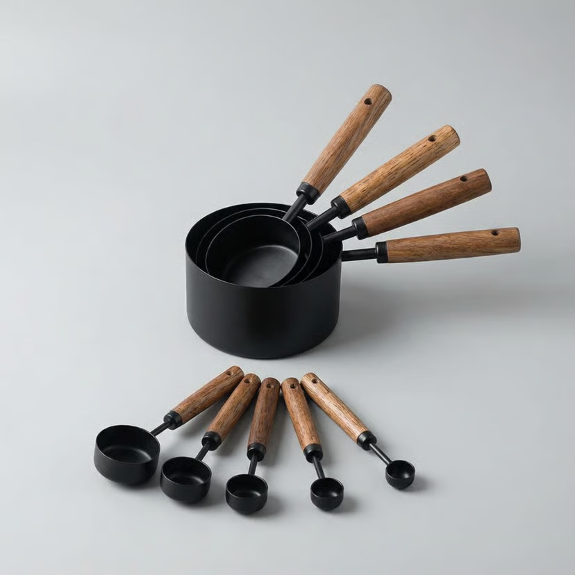 Set of black measuring cups and spoons with wooden handles on a light gray background