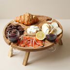 Wooden charcuterie board with croissant, cheese, cured meats, and glasses of red wine on a beige background.