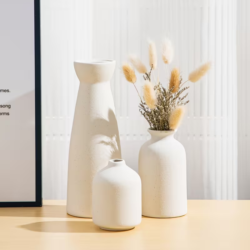 Three white ceramic vases on a wooden surface with a blurred background