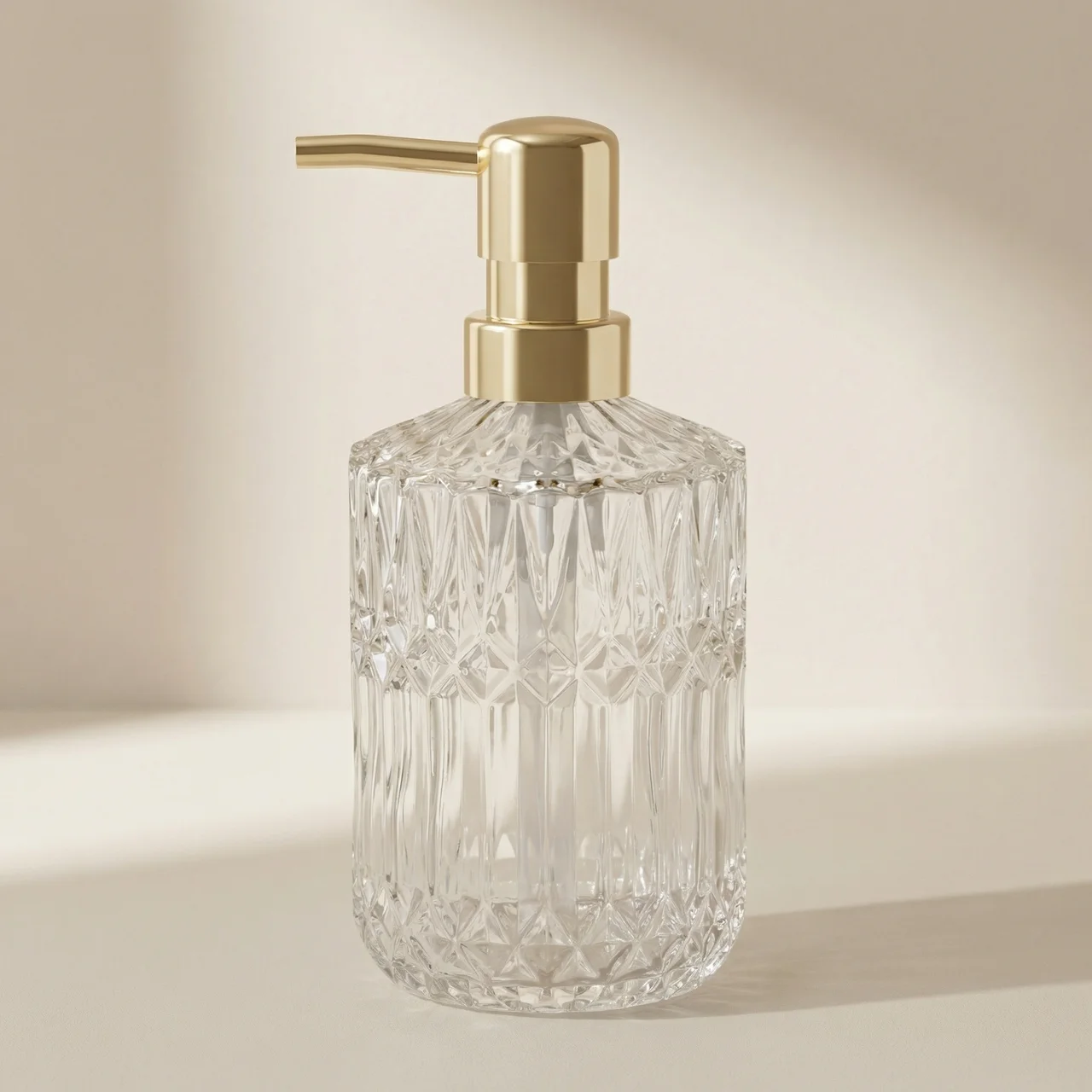 Clear glass soap dispenser with gold pump on a beige background