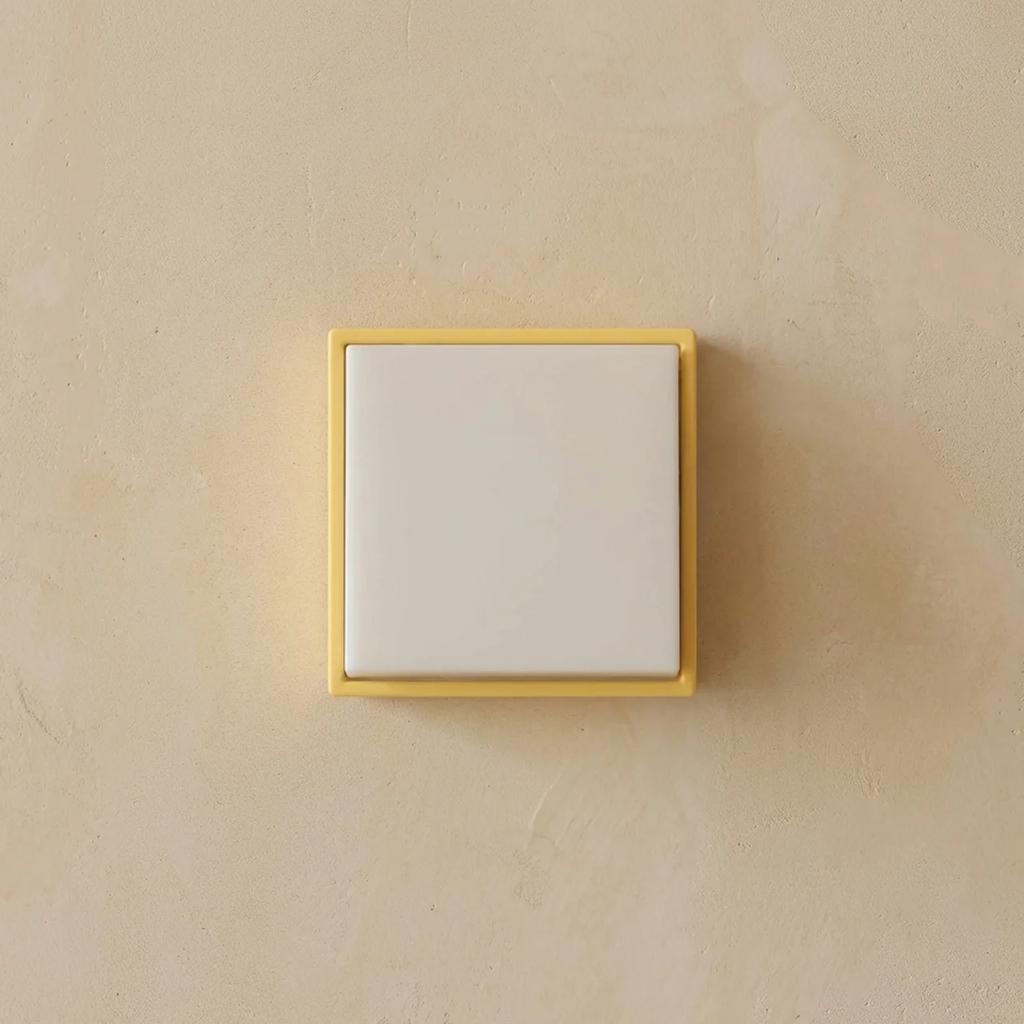 Square light switch with yellow frame on beige wall