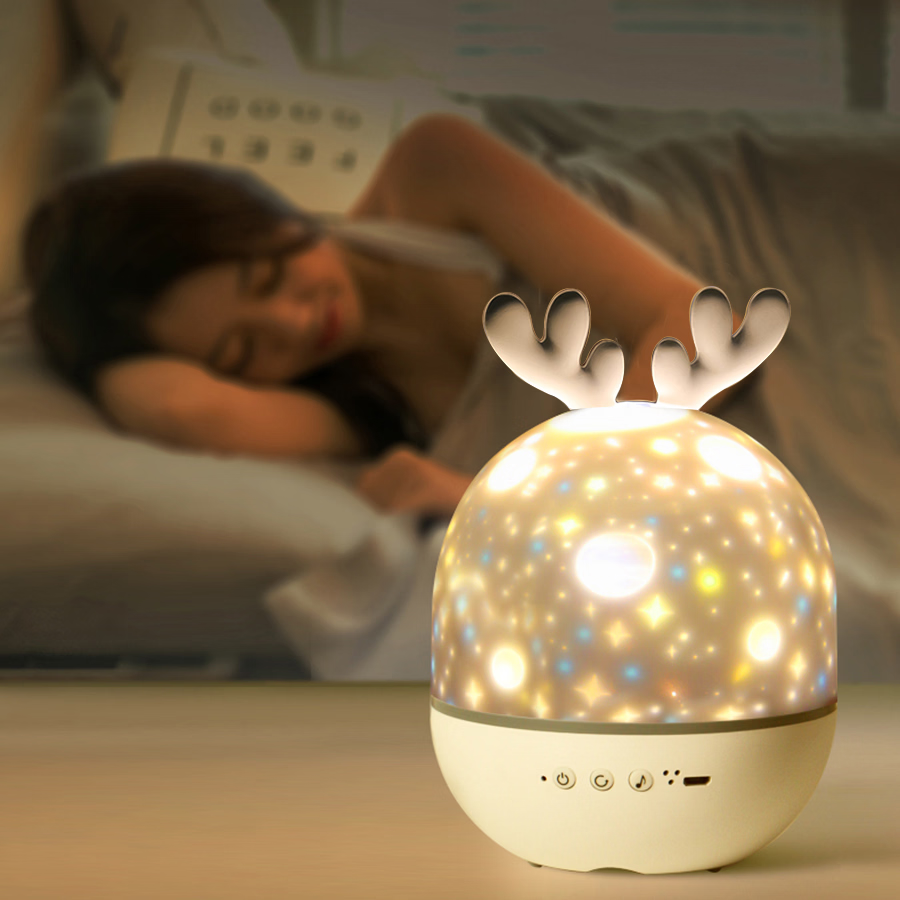 Decorative night light with reindeer antlers on a bedside table, with a person sleeping in the background.