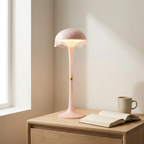 Pink table lamp on a wooden surface with an open book and a mug in a softly lit room.