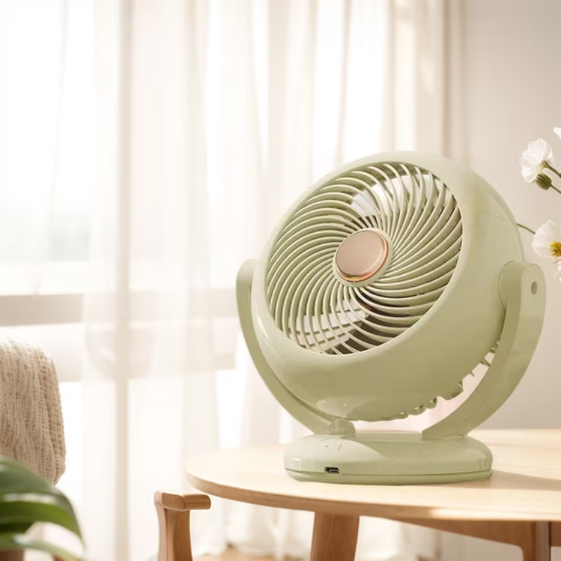 Green table fan on a wooden table with a blurred background