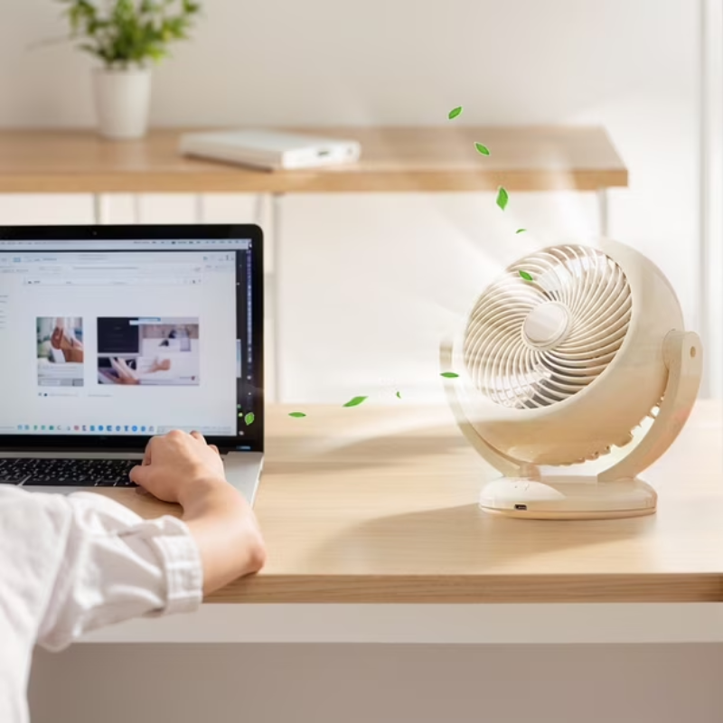 Person using a laptop with a small white fan on a desk