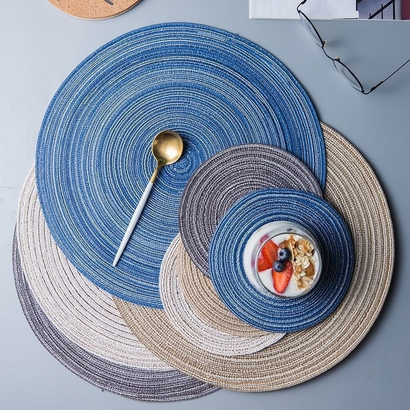 Set of round woven placemats in blue, gray, and beige on a flat surface.
