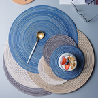 Set of round woven placemats in blue, gray, and beige on a flat surface.
