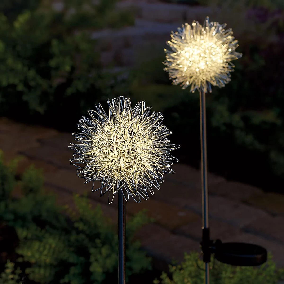 Two decorative solar lights shaped like dandelions on stakes with a blurred garden background.
