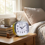 Alarm clock on a nightstand next to a bed with books and a mug.