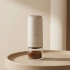 Manual coffee grinder with ground coffee on a beige surface
