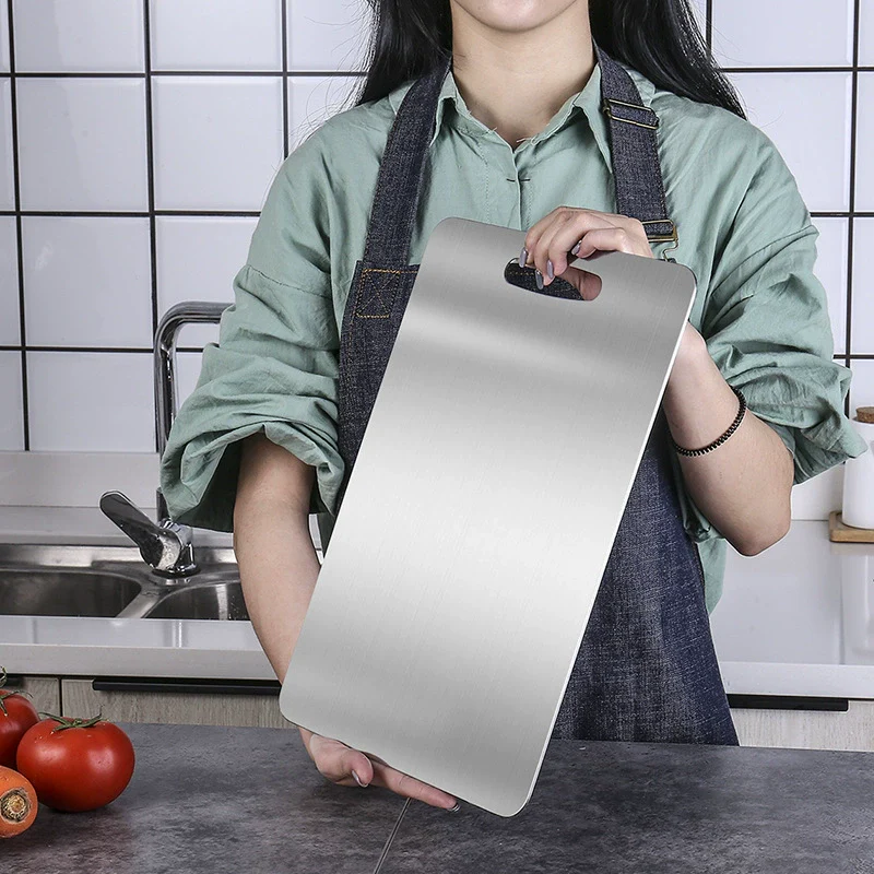 Person holding a metallic cutting board in a kitchen setting