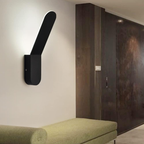 Modern black wall-mounted light fixture on a neutral wall with a bench in the foreground.