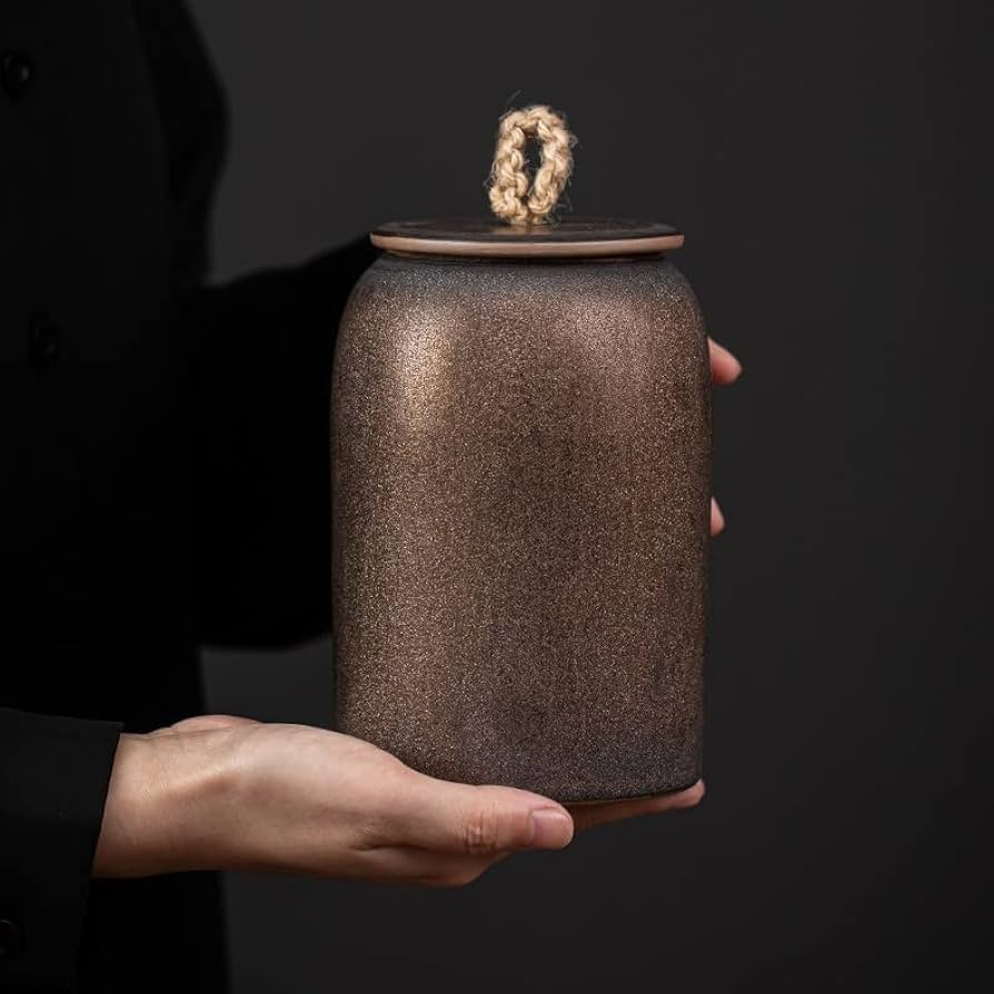 Person holding a textured brown jar with a small decorative object on a black background